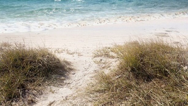 Une plage avec une eau d’un bleu limpide et un rivage sablonneux.