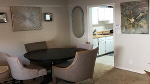 Un coin repas comprenant une table ronde et quatre chaises, un luminaire au plafond, un miroir fixé au mur et un tableau.