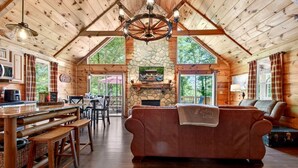 A log cabin interior with a stone fireplace, wooden furniture, and a dining area.