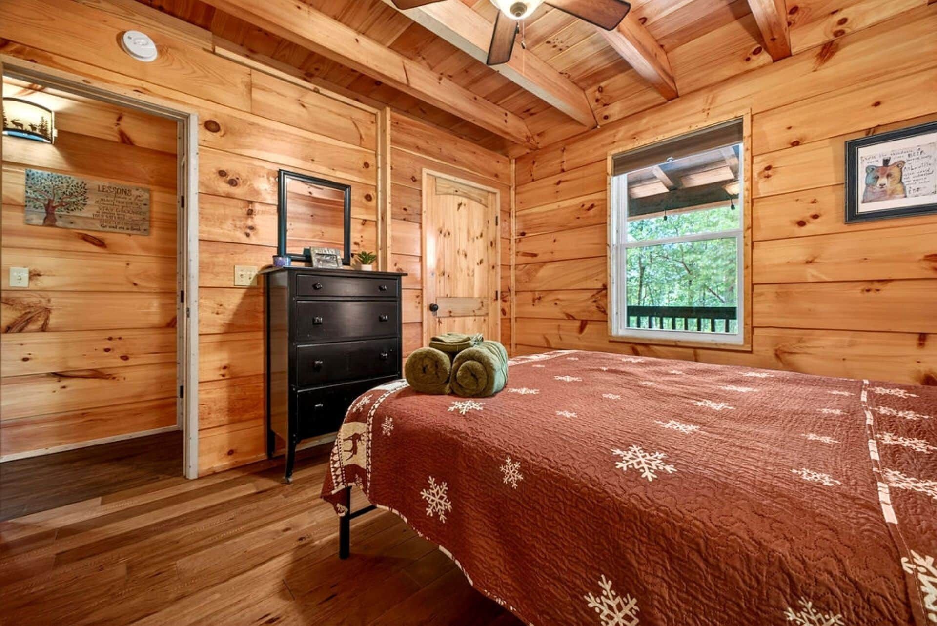 Un dormitorio de cabaña de madera con cama, cómoda y ventana.