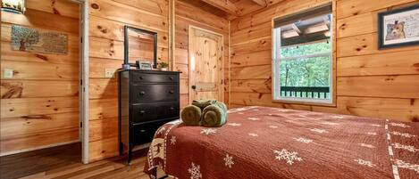 Un dormitorio de cabaña de madera con cama, cómoda y ventana.