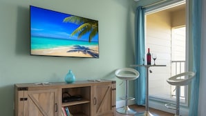 Una habitación con un armario de madera, un cuadro de una playa, dos taburetes altos y una ventana con cortinas.