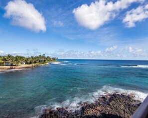 A coastal landscape with clear skies, a rocky shoreline, and a distant shoreline with vegetation. - Sleep to Surf Sounds & Trade Winds [or AC!] While Enjoying Your Oceanfront Home. (poipu)