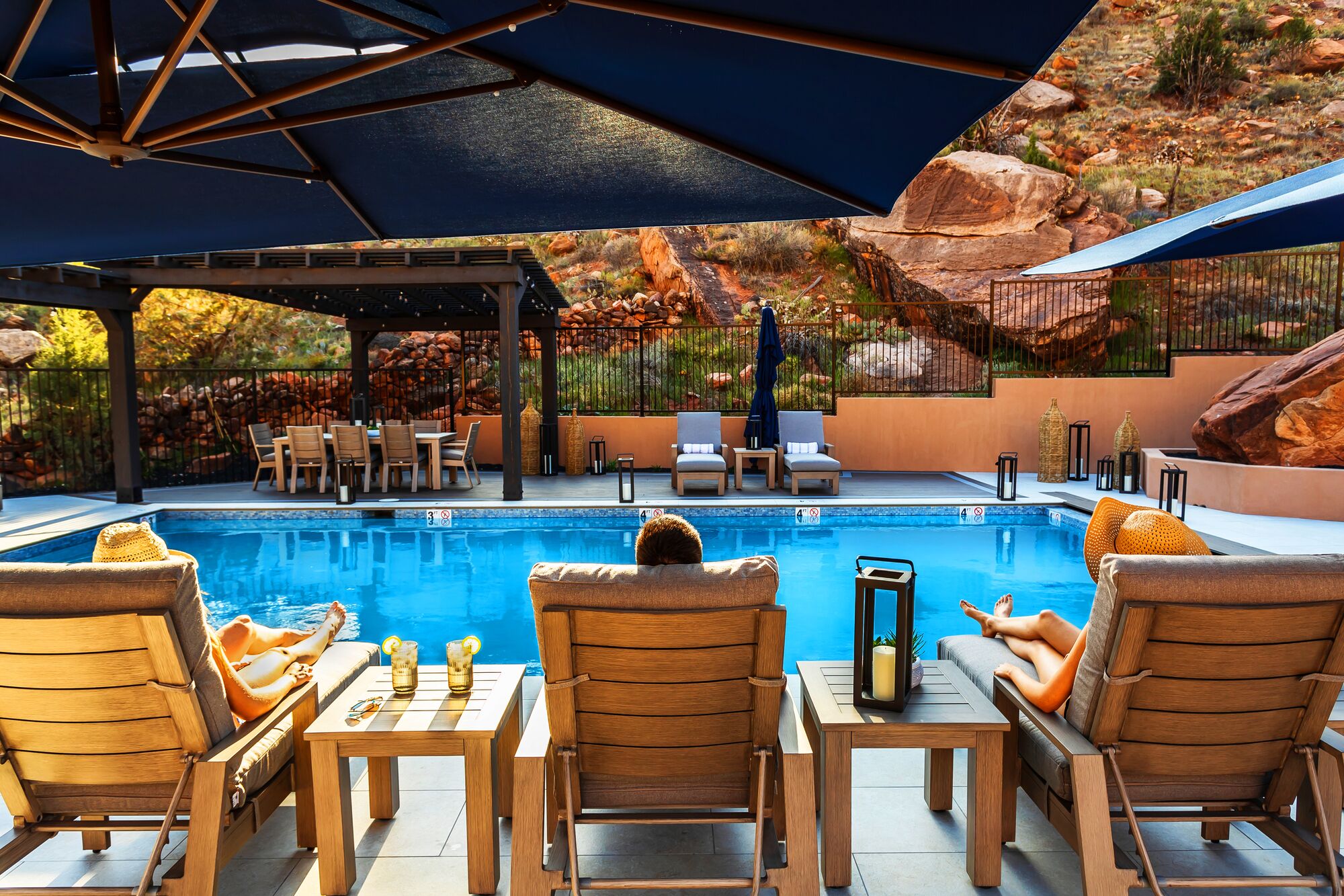 Un espace aménagé au bord de la piscine, avec des chaises longues, un coin salon abrité et une vue sur un paysage rocheux.