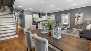Ein modernes Wohnzimmer mit einem Holzespeisetisch, grau gepolsterten Stühlen, einem grauen Sofa und einer Treppe, die in einen Küchenbereich führt.