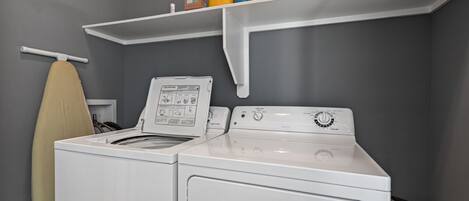 Un área de lavandería con lavadora, secadora y estante con productos de limpieza.