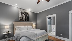 Ein Schlafzimmer mit einem großen Bett, zwei Nachttischen mit Lampen, einem Deckenventilator und einem durch eine offene Tür einsehbaren Badezimmer.