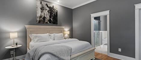 Un dormitorio con una cama grande, dos mesitas de noche con lámparas, un ventilador de techo y un baño visible a través de una puerta abierta.