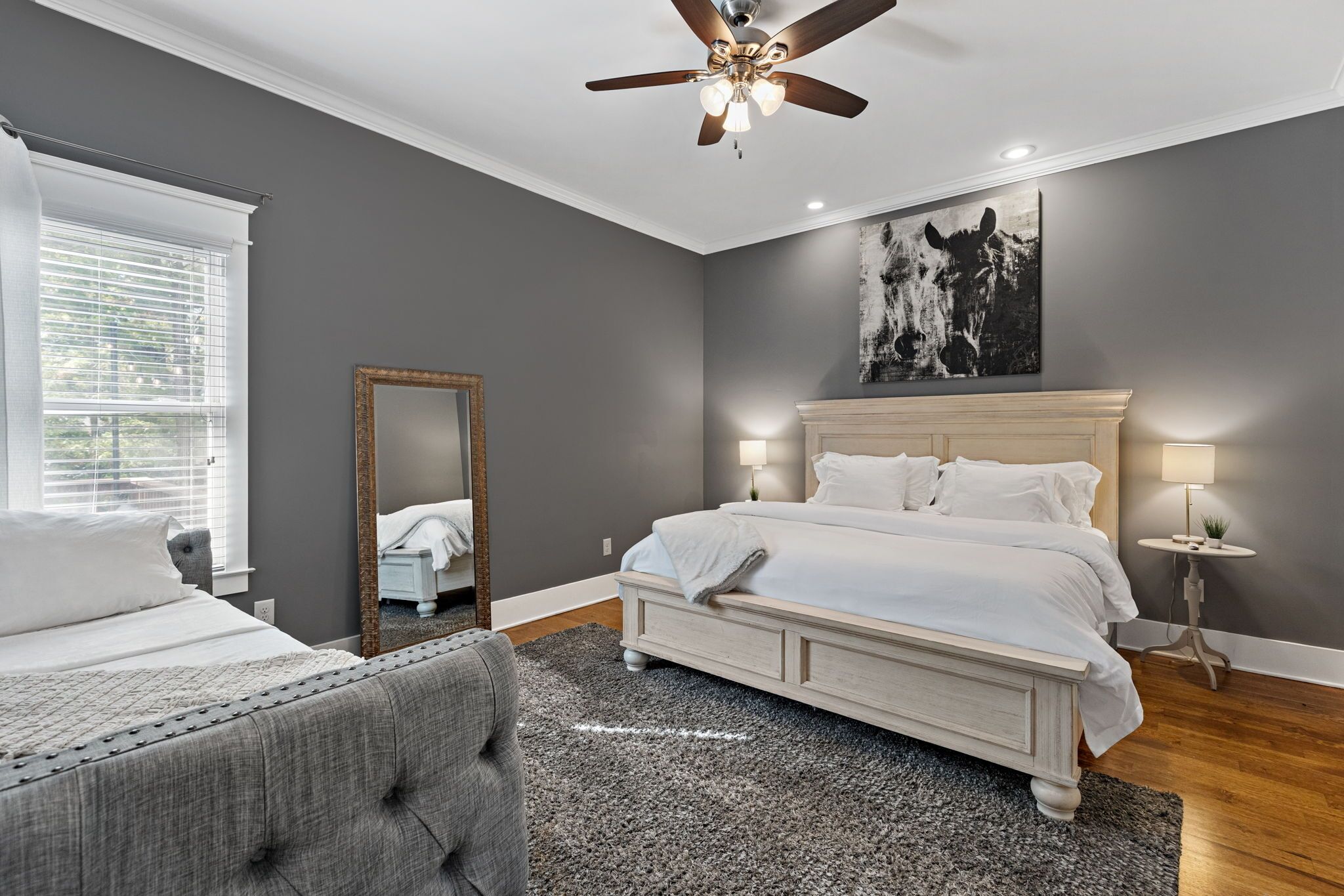 A bedroom with a large bed, a ceiling fan, a mirror, and a painting on the wall.