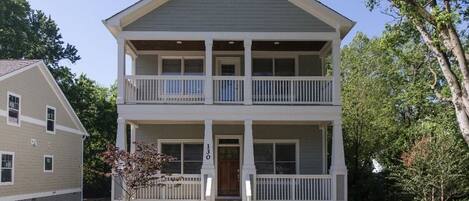 A two-story building with a front porch and a small tree in front.