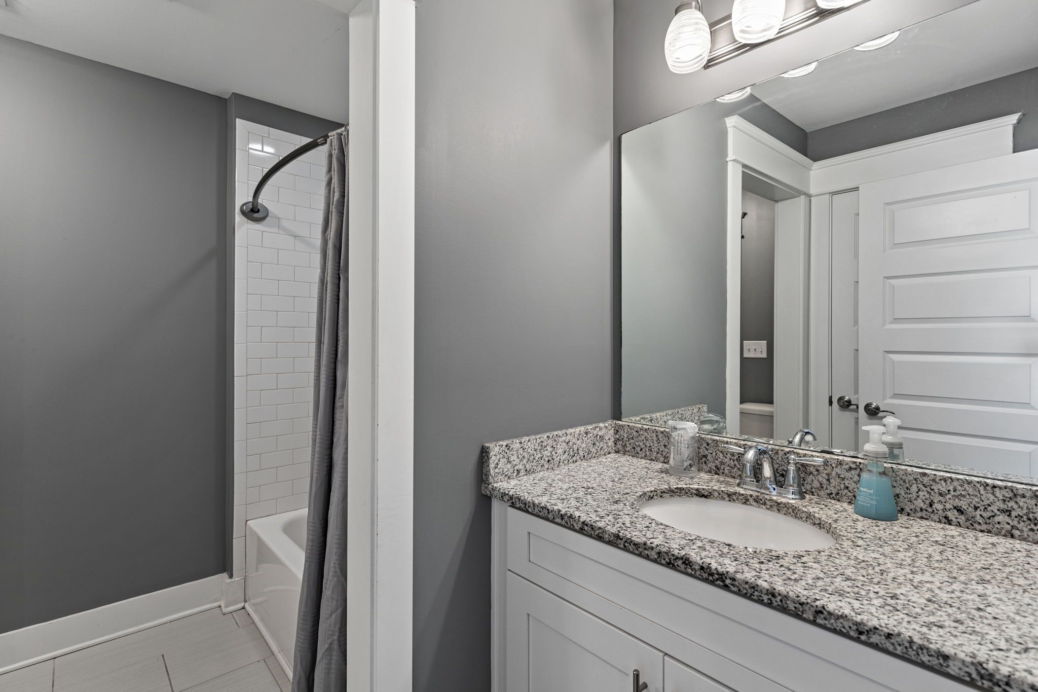 A bathroom with a shower, a sink with a mirror, and a door.