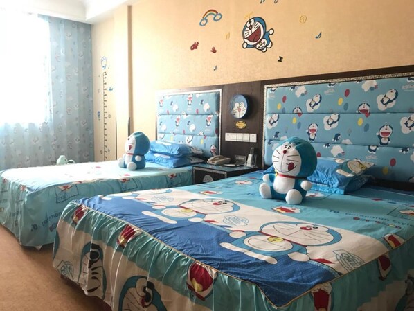 Habitación de hotel con dos camas, cada una con una colcha temática de Doraemon en azul y blanco. Hay adhesivos de pared con personajes de Doraemon, un reloj y una mesita con un teléfono y un vaso.