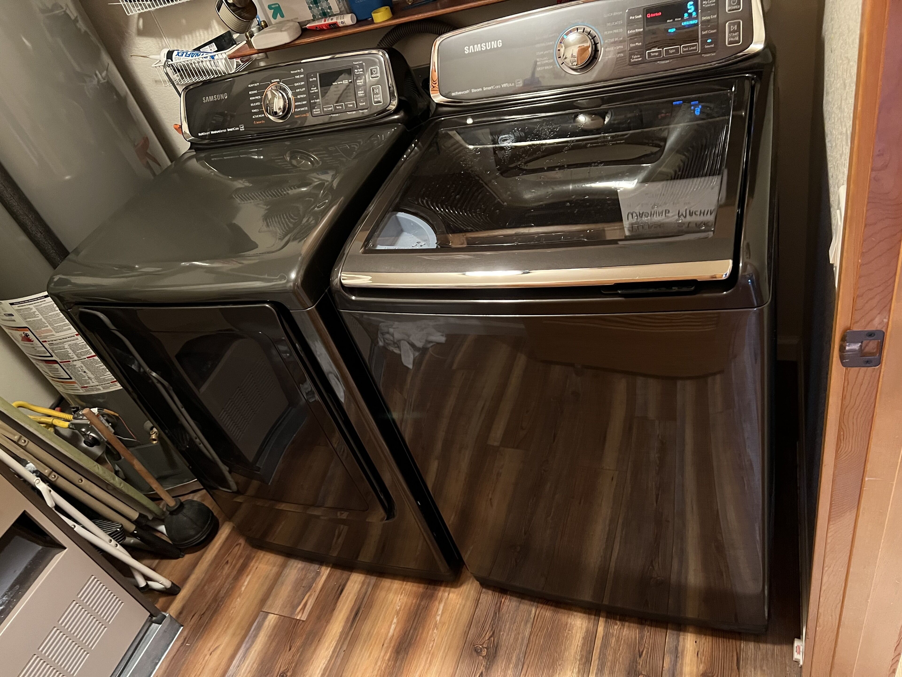 Un appareil compact combinant lave-linge et sèche-linge, doté d’un panneau de commande, installé dans une petite buanderie au sol en bois.