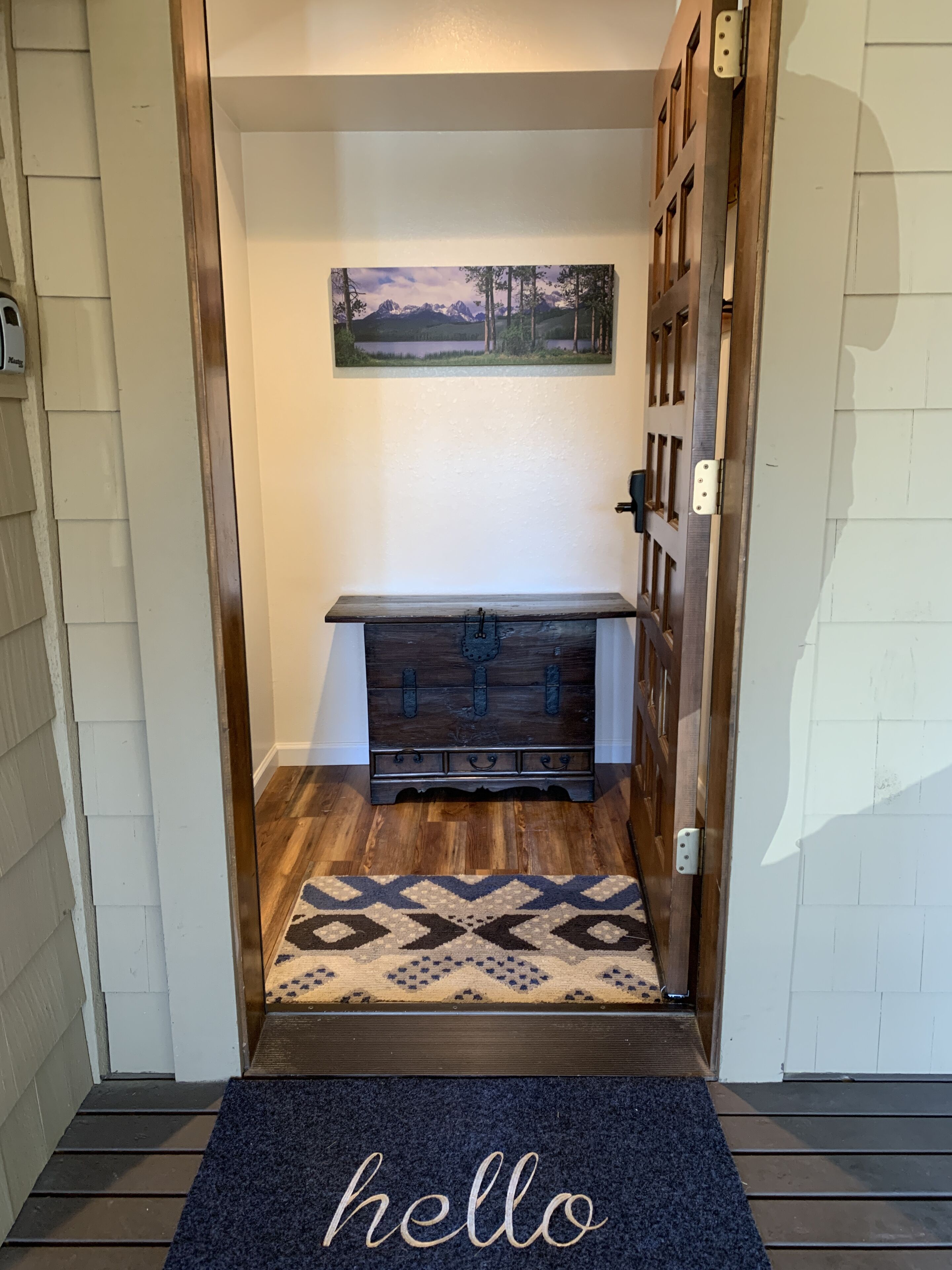 A wooden bench with a rustic design, a welcome mat with the word "hello," and a framed landscape painting on the wall.