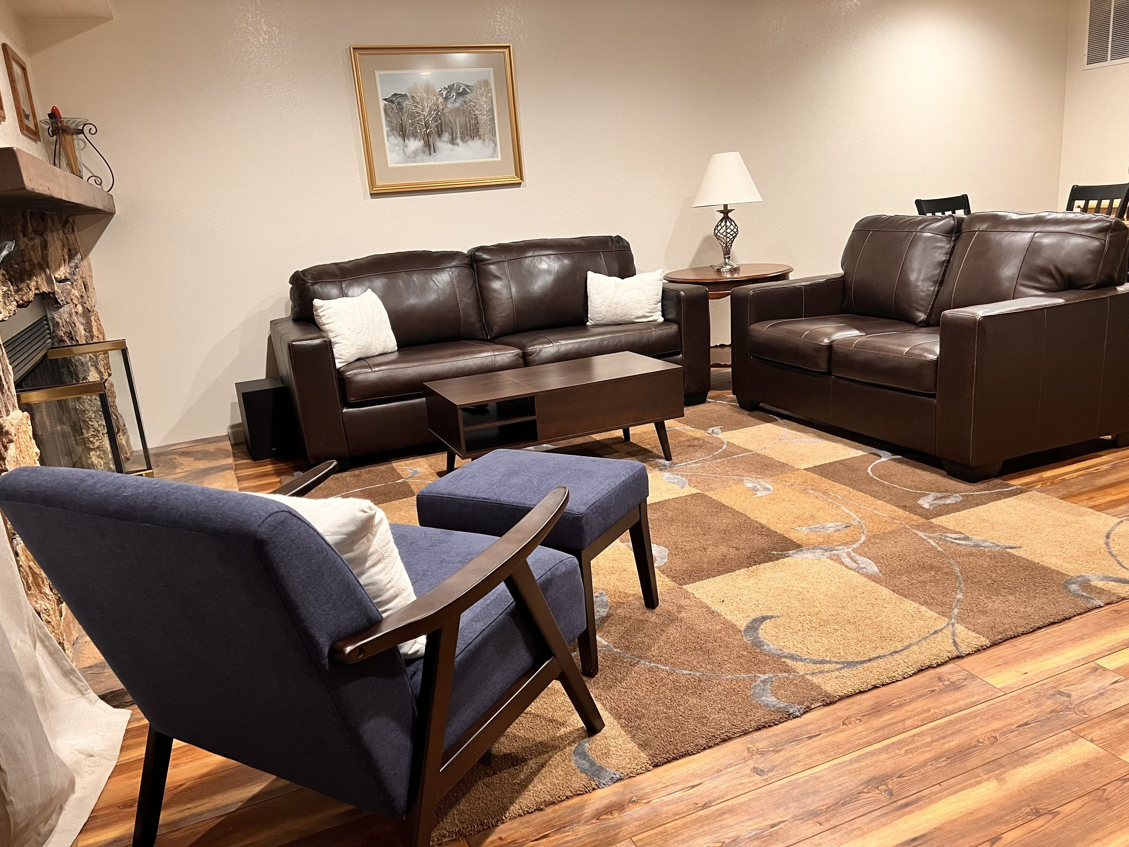 Ein Wohnzimmer mit braunem Ledersofa, einem blauen Sessel, einem Holztisch und einem gemusterten Teppich.