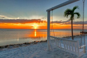 Una hamaca en la playa con una palmera, con vista al mar tranquilo al atardecer.