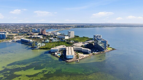 Vista aérea de una ciudad costera con un puerto deportivo, rascacielos y una pequeña isla con varias construcciones.