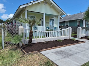 A residential house with a front porch, a fenced yard, and a palm tree.