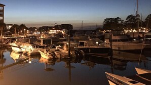 A marina at dusk with boats docked and calm water reflecting the lights.