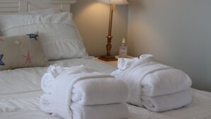 A neatly made bed with white linens and a starfish pillow, a bedside lamp, and a bottle of lotion on a nightstand.