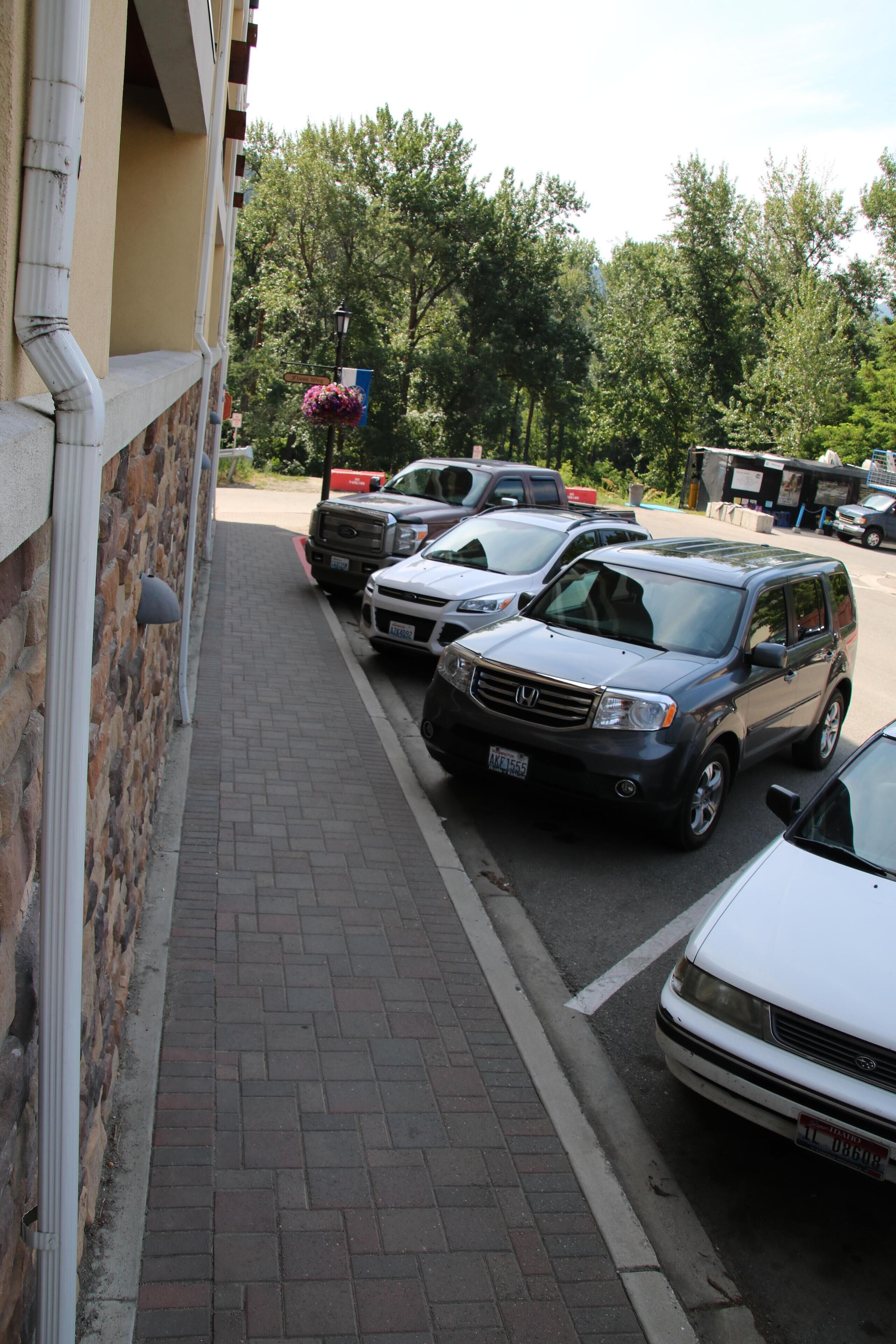A parking lot with several cars parked along a brick sidewalk.