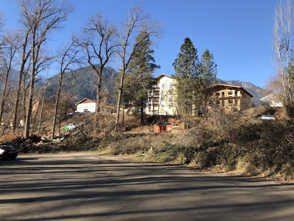 Un camino rural con un edificio rodeado de árboles y montañas al fondo.