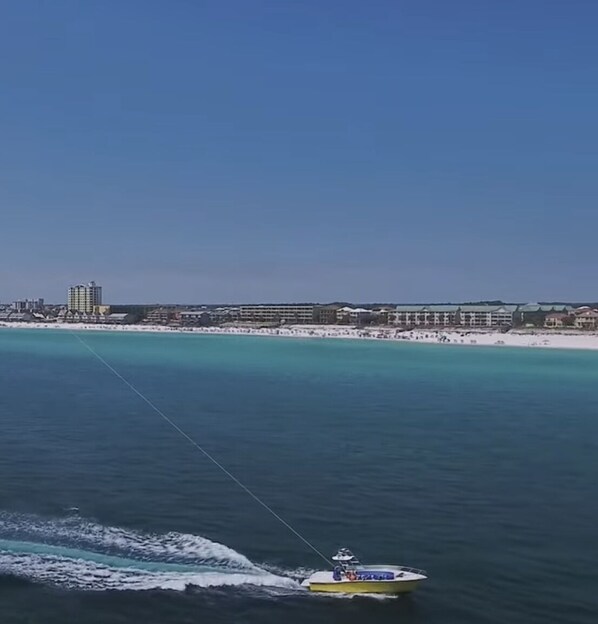 Paesaggio costiero con una barca sull'acqua, una spiaggia e edifici sullo sfondo, sotto un cielo sereno.