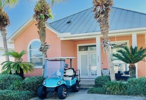 Een huis met een blauwe golfkar voor de deur, omringd door palmbomen en goed onderhouden struiken.
