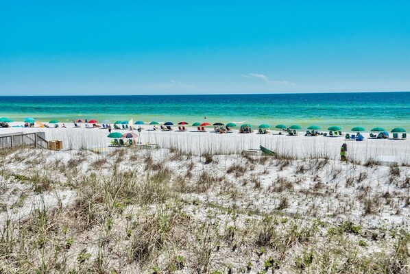 Een strand met wit zand, groene parasols en een houten looppad.