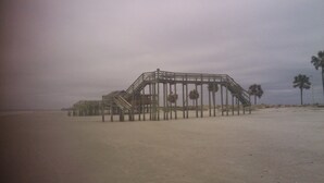 A beach with a wooden structure, possibly a pier or boardwalk, and palm trees in the background. - Beach/Pier/Restaurants/Shopping/Outstanding Location...100yards to All! Parking  (Folly Beach)
