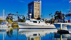 A marina with a white yacht named 'OCEANSIDE 95' docked, surrounded by other boats and a tall building in the background.