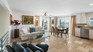 A spacious living area with a sofa, coffee table, dining table, and chairs. A kitchen with cabinets and a dishwasher is visible.