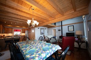 A spacious living area with a high wooden ceiling, a dining table set for four, and a red armchair.