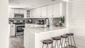 Une cuisine moderne avec des meubles blancs, un îlot central doté de tabourets, un four à micro-ondes, une cuisinière et une machine à café.