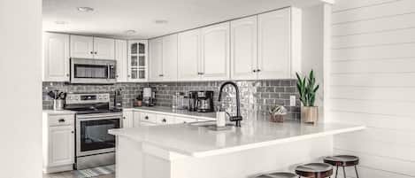 A modern kitchen with white cabinets, a central island with stools, a microwave, stove, and a coffee maker.