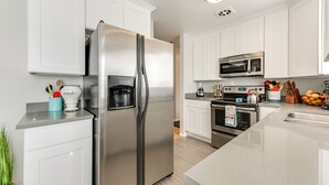 Una cocina moderna con armarios blancos, electrodomésticos de acero inoxidable, dispensador de agua y microondas.