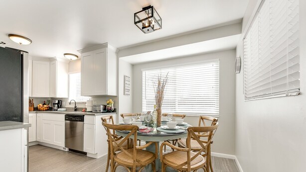 Una cocina moderna con armarios blancos, una mesa de comedor con cuatro sillas y un ventanal con persianas.