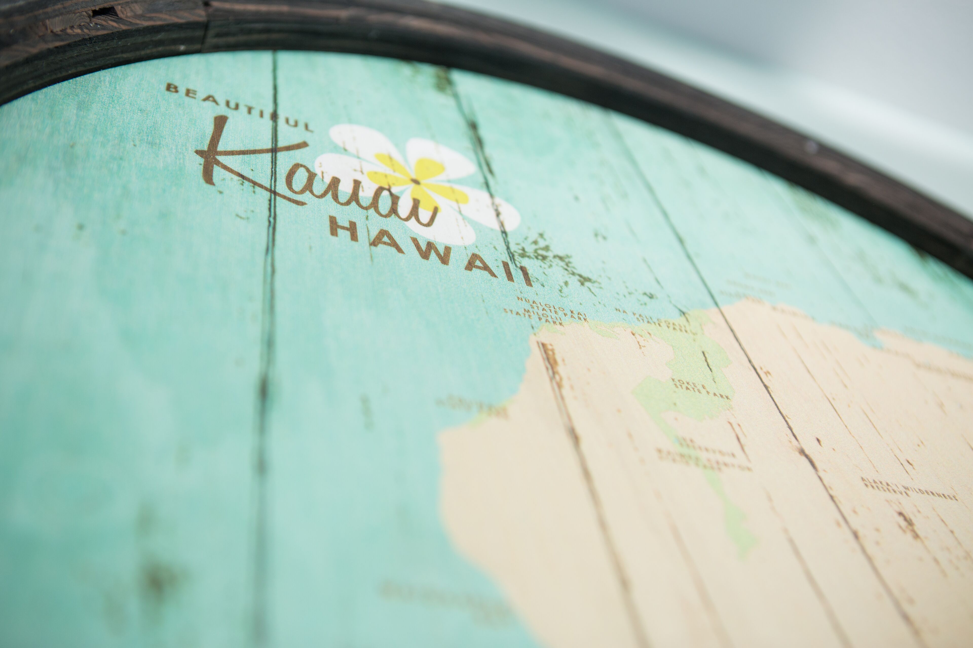 Een detailopname van een houten oppervlak met de tekst 'Kauai Hawaii' en een bloemlogo.