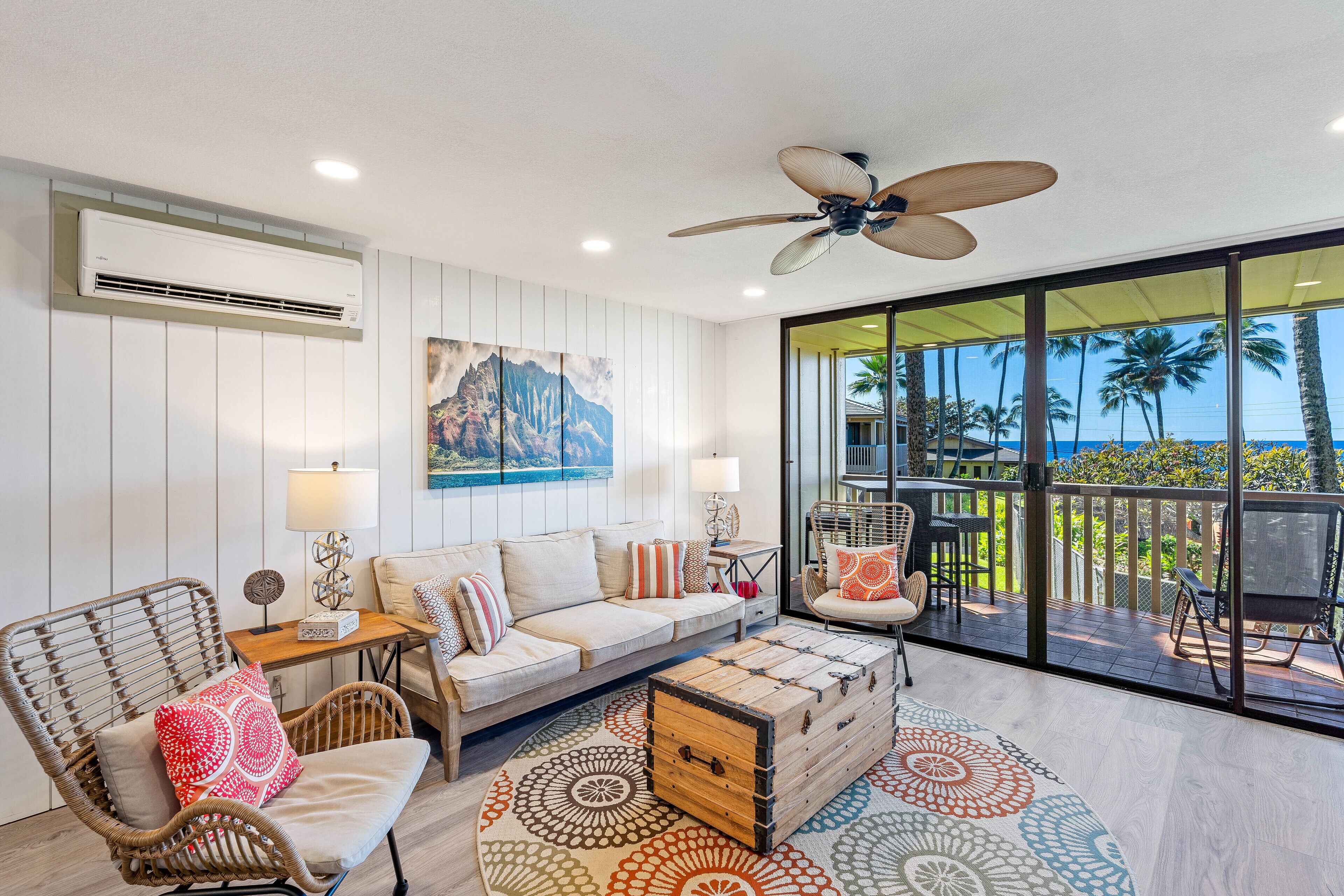 A spacious living room with a sofa, chairs, a coffee table, and a view of the ocean through large sliding doors.