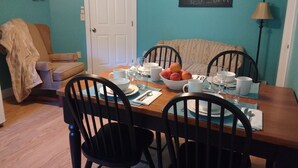Comedor con una mesa de madera dispuesta para cuatro personas, rodeada de sillas negras. Un frutero y vajilla blanca se encuentran sobre la mesa.