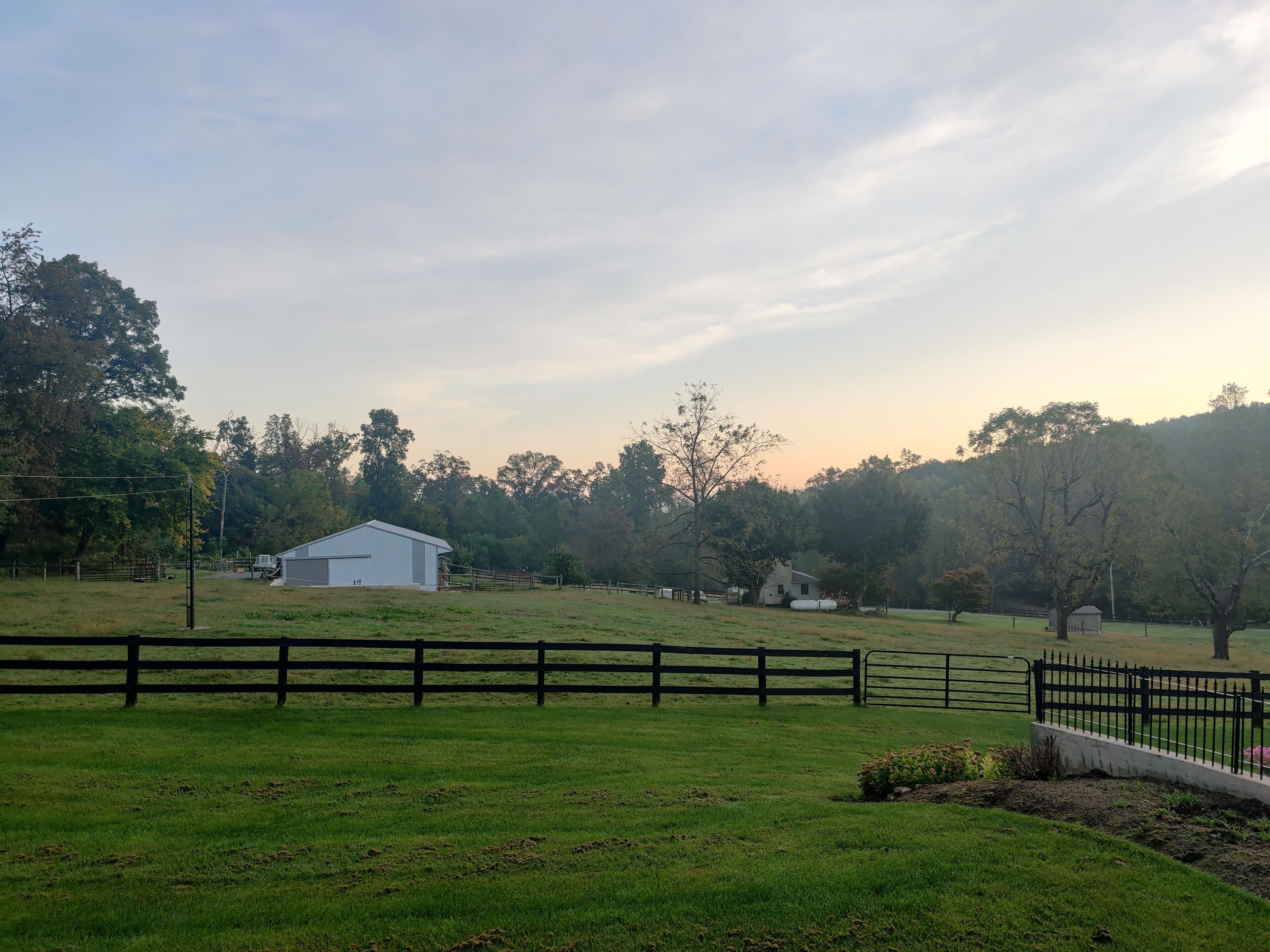 A rural landscape with a fenced field, a white building, and trees in the background.