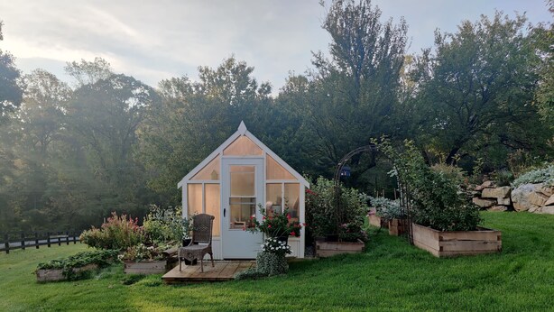 Una pequeña estructura de madera con techo inclinado, rodeada de un jardín bien cuidado con diversas plantas y flores.