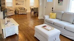 A living room with a sofa, ottoman, and a dining area with a table and chairs. - Fort Grounds Cottage Across from City Beach, Park & Downtown! (Coeur d'Alene)