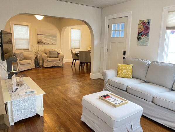 A living room with a sofa, ottoman, and a dining area with a table and chairs.
