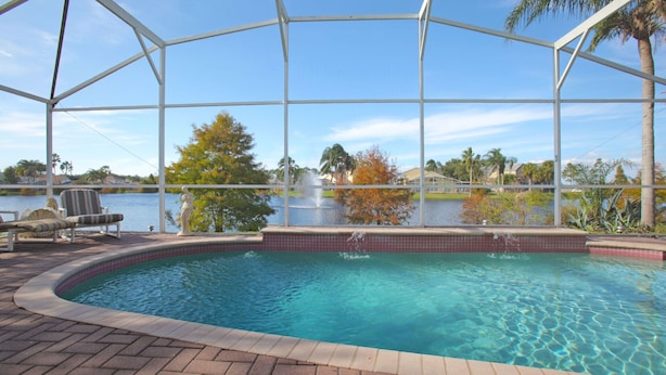 A swimming pool with a view of a lake and palm trees, surrounded by a covered area with lounge chairs. - Mickey's Lake Villa 2 only a few miles from Disney  (Kissimmee)