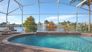 Piscina con vista a un lago y palmeras, rodeada por una zona cubierta con sillas de descanso.
