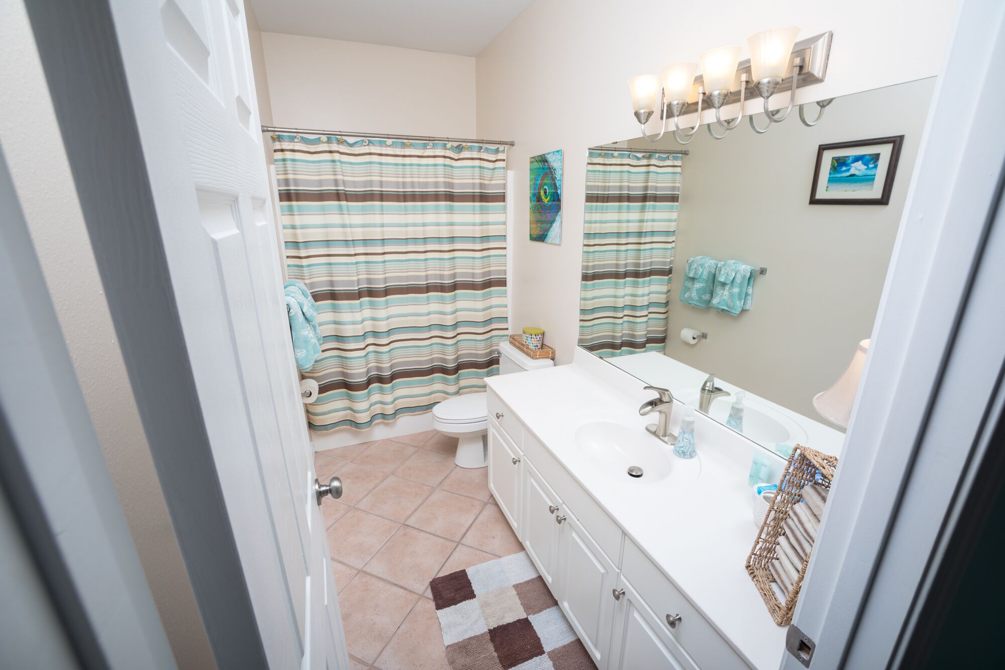 A bathroom with a white vanity, a large mirror, and striped shower curtains.