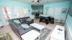 A living room with a black leather sofa, a white coffee table, and a dining table with chairs. - WALK STEPS TO BEACH AND POOL.  GREAT LOCATION!  close to activities and shopping (Destin)