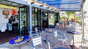 An outdoor cafe with tables and chairs, a blue awning, and a glass storefront. - WALK STEPS TO BEACH AND POOL.  GREAT LOCATION!  close to activities and shopping (Destin)