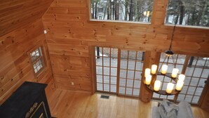 Ein Holzblockhaus-Interieur mit Kamin, großen Fenstern und einer Hängeleuchte.